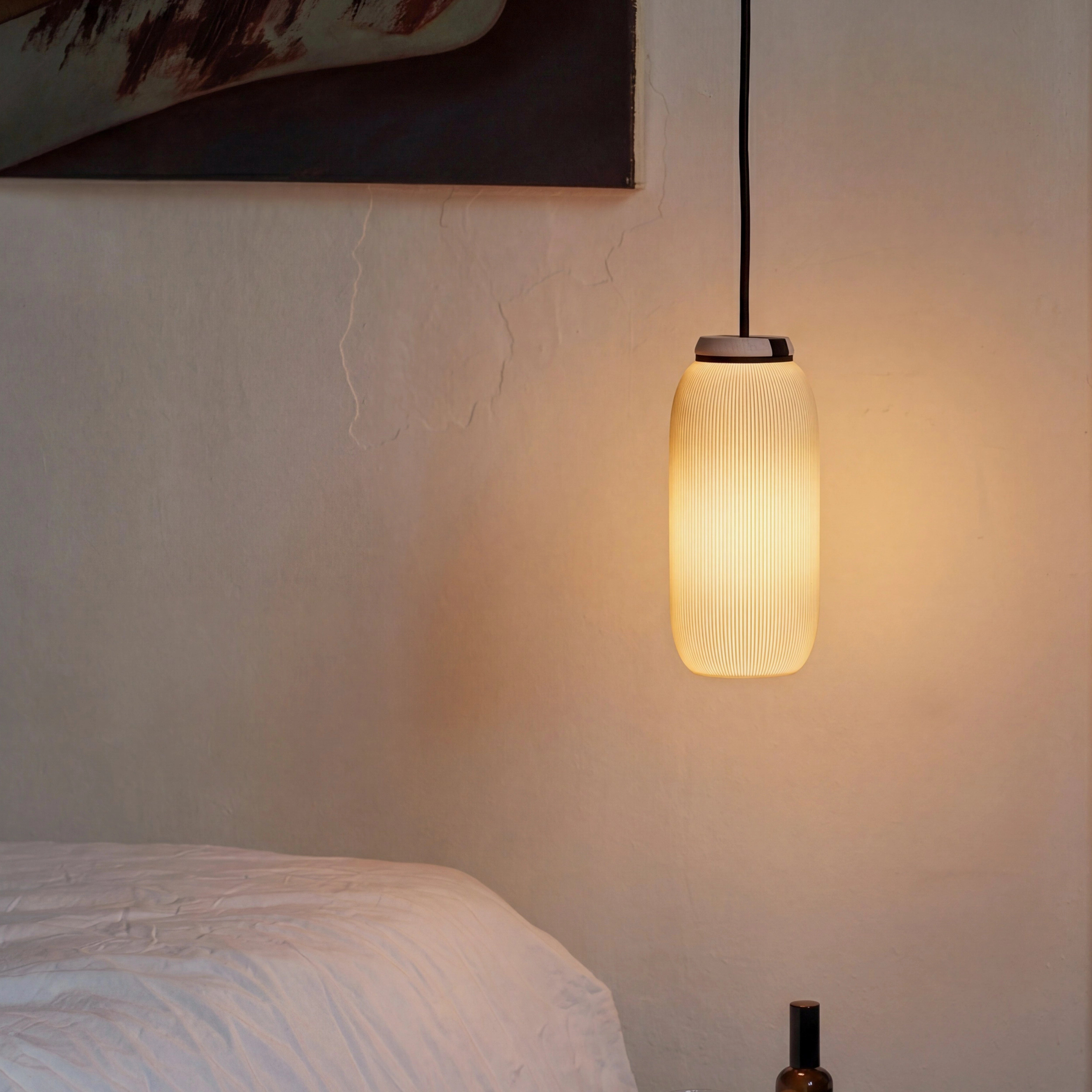 Pendelleuchte PILLE mit warmem Licht über Bett vor Lehmwand mit Kunstdruck im Schlafzimmer